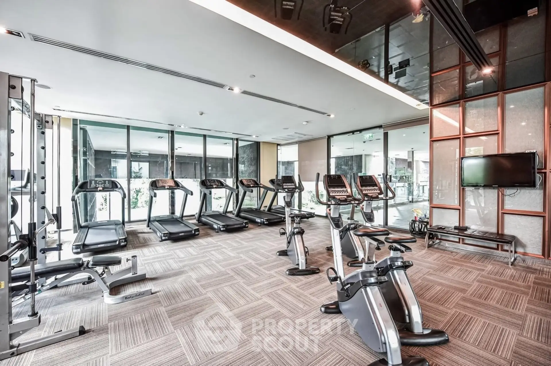 Modern gym with state-of-the-art equipment and floor-to-ceiling windows in luxury apartment building.