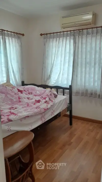 Cozy bedroom with wooden flooring and natural light from multiple windows.