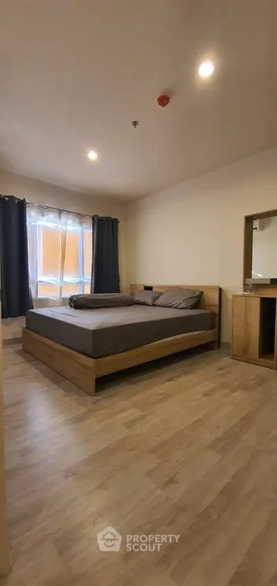 Spacious bedroom with modern wooden bed, matching sideboard, and elegant dark curtains complementing the warm-toned flooring.