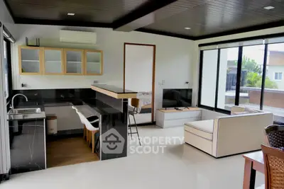 Modern open-layout living room with sleek kitchen and large windows offering natural light.