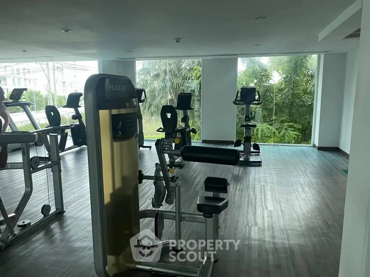Modern gym with exercise equipment and large windows overlooking greenery.
