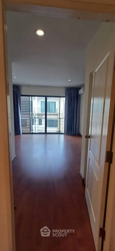 Spacious empty room with wooden flooring and large windows leading to a balcony.