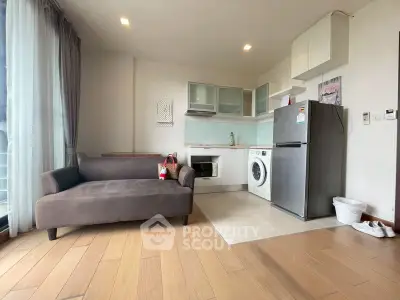 Modern living room with open kitchen, featuring a cozy sofa, washing machine, and stainless steel fridge.