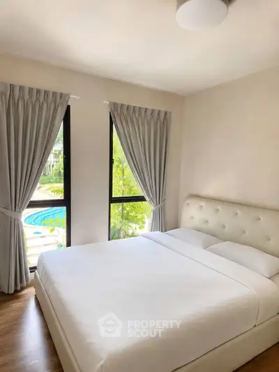 Bright bedroom with large windows and pool view, featuring elegant curtains and a plush bed.