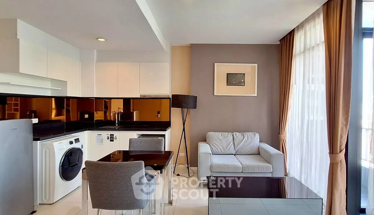 Modern living room with open kitchen, featuring sleek furniture and large windows for natural light.