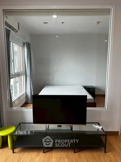 Modern bedroom with large window and sleek TV setup, perfect for urban living.