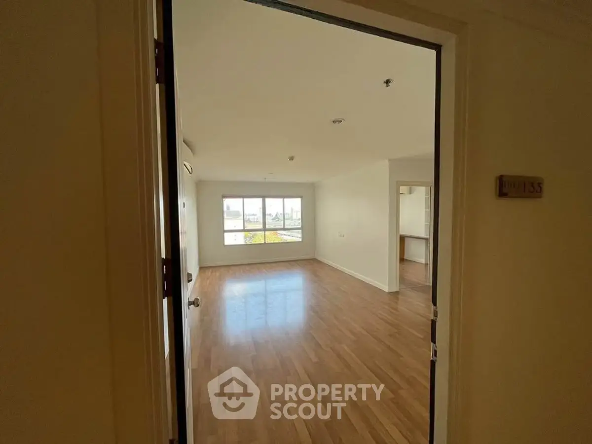 Spacious empty room with wooden flooring and large window offering natural light.