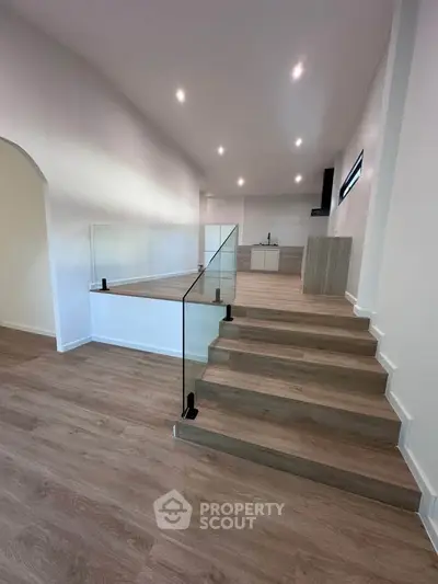 Modern open-plan living space with sleek wooden flooring and glass railing, perfect for contemporary living.