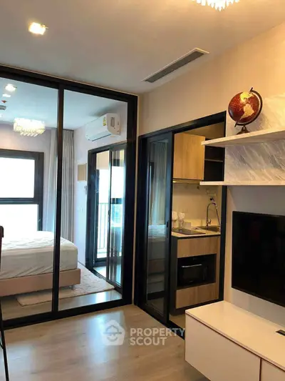 Modern apartment interior with glass partition, cozy bedroom, and compact kitchen area.
