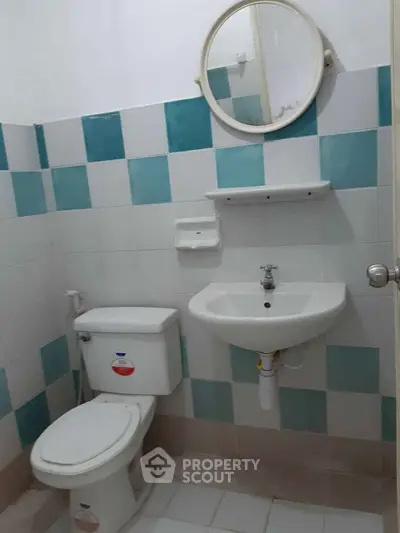 Compact bathroom with modern fixtures and blue-tiled walls, featuring a round mirror and white sink.