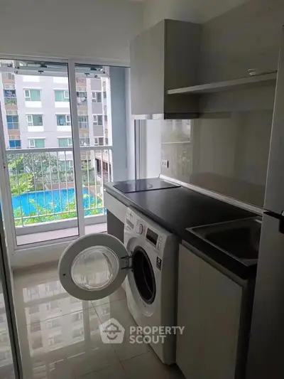 Modern kitchen with washing machine and pool view in a high-rise apartment.