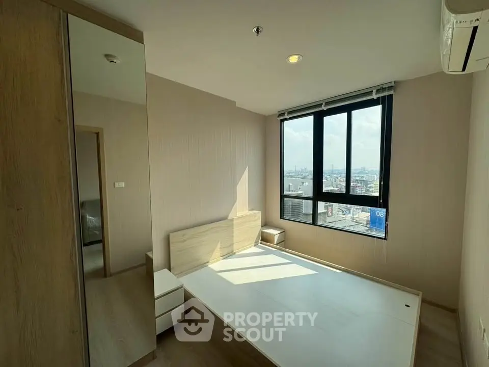 Modern bedroom with large window offering city views, featuring minimalist design and ample natural light.