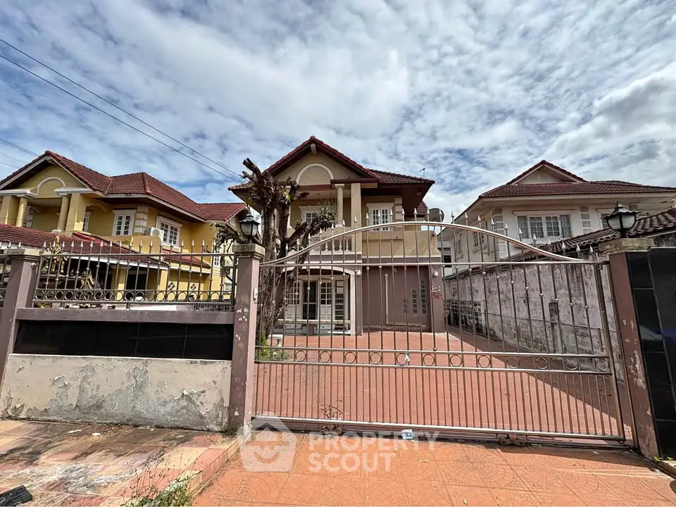 Spacious two-story house with gated entrance and tiled driveway under a cloudy sky.