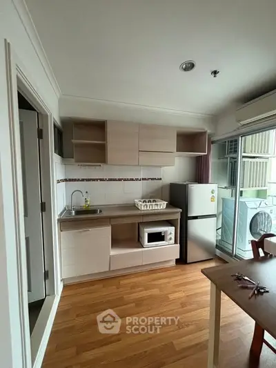Modern compact kitchen with wooden flooring, featuring a fridge, microwave, and ample storage space.