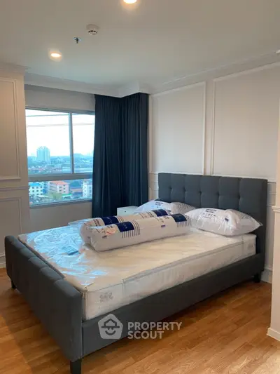 Spacious bedroom with large window and city view, featuring elegant decor and wooden flooring.