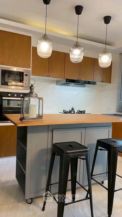 Modern kitchen with island, pendant lights, and gas stove, featuring sleek cabinetry and stylish stools.
