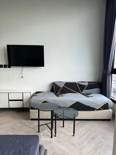 Modern living room with stylish sofa, wall-mounted TV, and chic glass tables in a bright apartment.