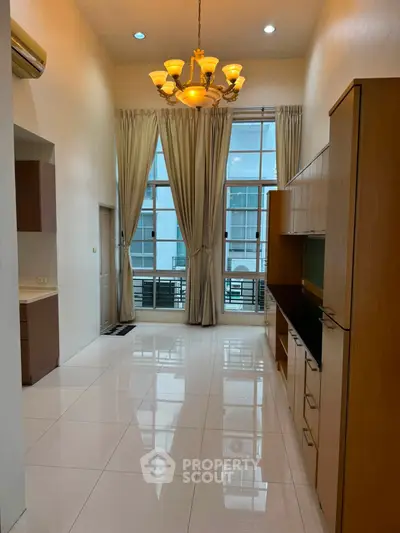 Spacious high-ceiling living room with elegant chandelier and large windows.
