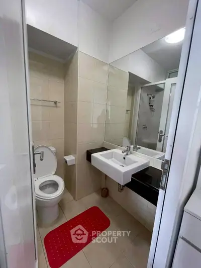 Modern bathroom with sleek fixtures and red mat, featuring a spacious mirror and contemporary design.
