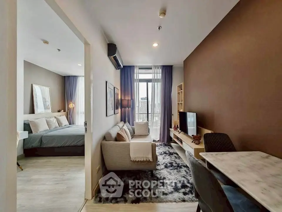 Modern open-plan living room with cozy seating and stylish decor, leading to a bright bedroom with large windows.