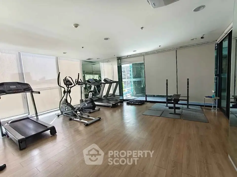Spacious gym with modern equipment and large windows in a luxury building.