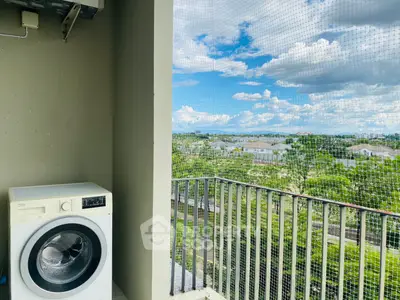 Spacious balcony with washing machine and scenic view of lush greenery and blue skies.