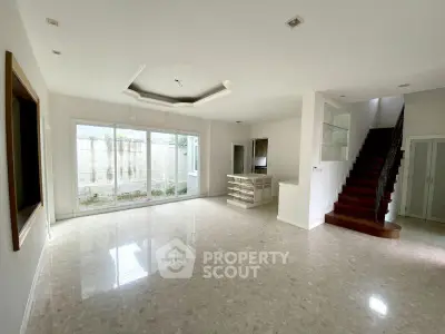 Spacious open-plan living room with large windows and elegant staircase