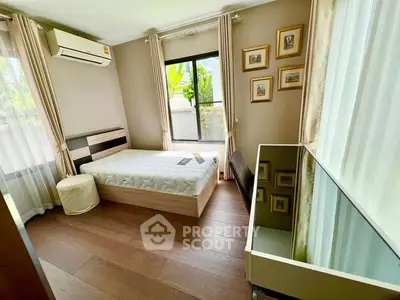 Cozy bedroom with wooden flooring and ample natural light, featuring modern decor and air conditioning.