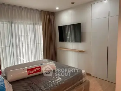 Modern bedroom with wall-mounted TV and large window, featuring sleek storage solutions.