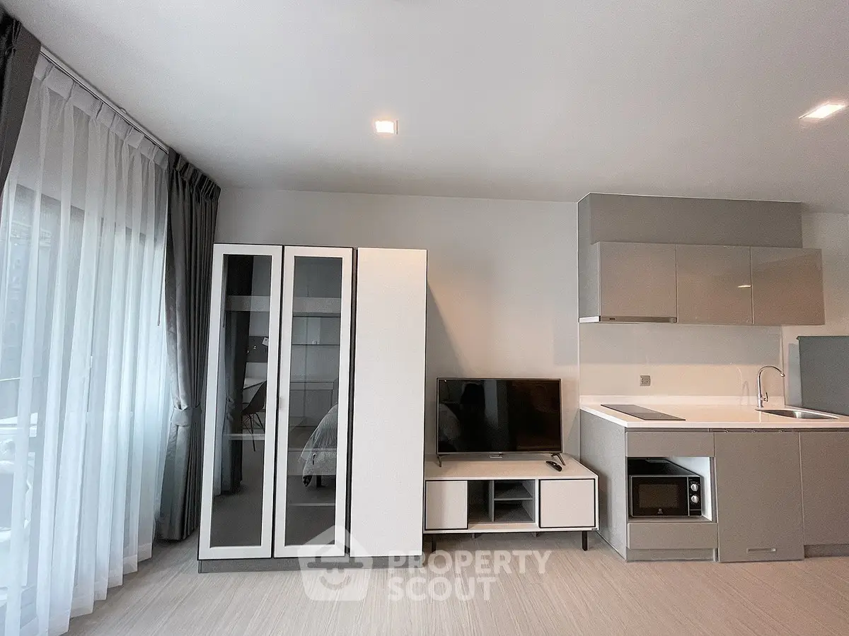 Modern studio apartment with sleek kitchen and stylish living area, featuring floor-to-ceiling windows and contemporary decor.
