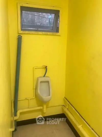 Compact yellow bathroom with urinal and small window, ideal for minimalist spaces.