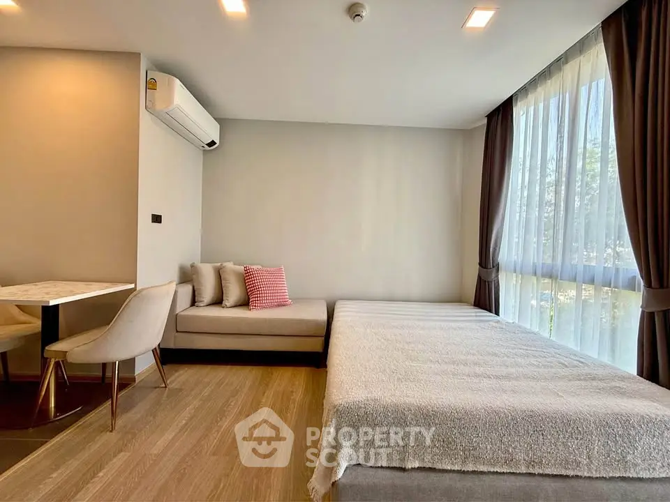 Modern studio apartment with cozy seating and large window for natural light.