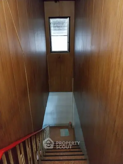Narrow staircase with wooden paneling and small window, ideal for compact spaces.