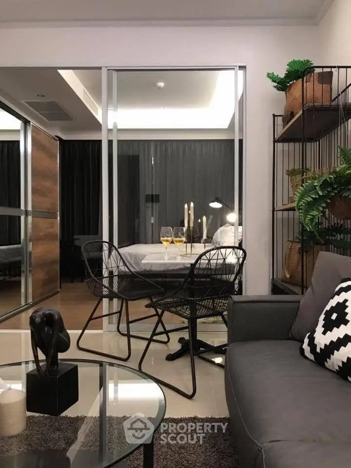 Modern living room with stylish decor and glass partition leading to bedroom, featuring elegant furniture and ambient lighting.