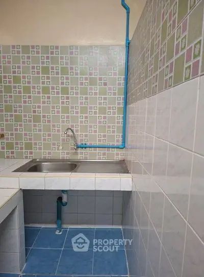 Compact kitchen with tiled walls and single sink, featuring a unique blue pipe design.