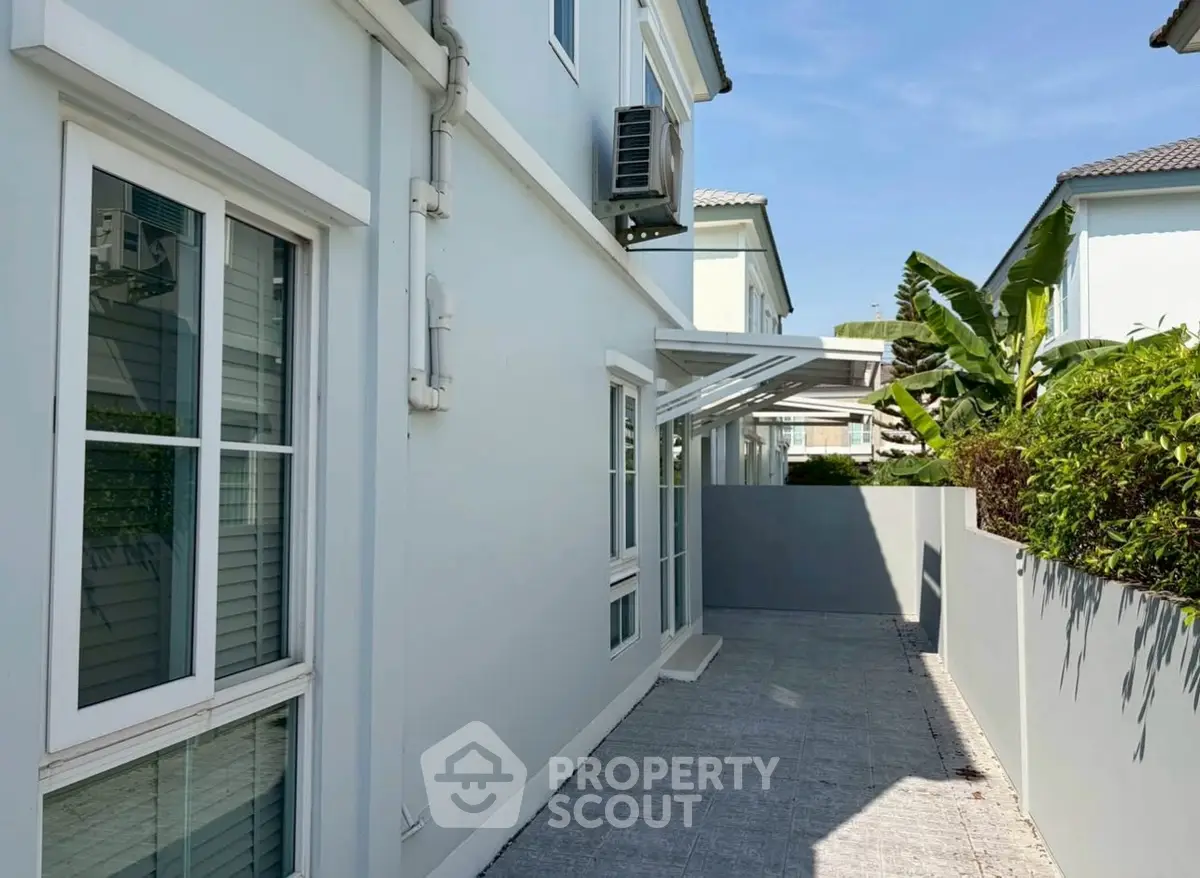 Modern exterior of a light blue house with lush greenery and paved walkway.