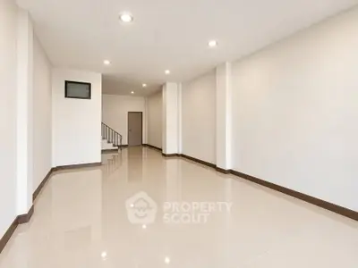 Spacious empty room with glossy tiled floors and staircase, ideal for customization.