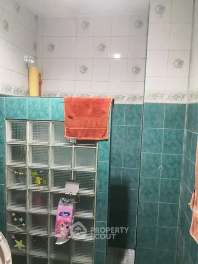 Charming bathroom with teal tiles and glass block wall, featuring a cozy and functional design.