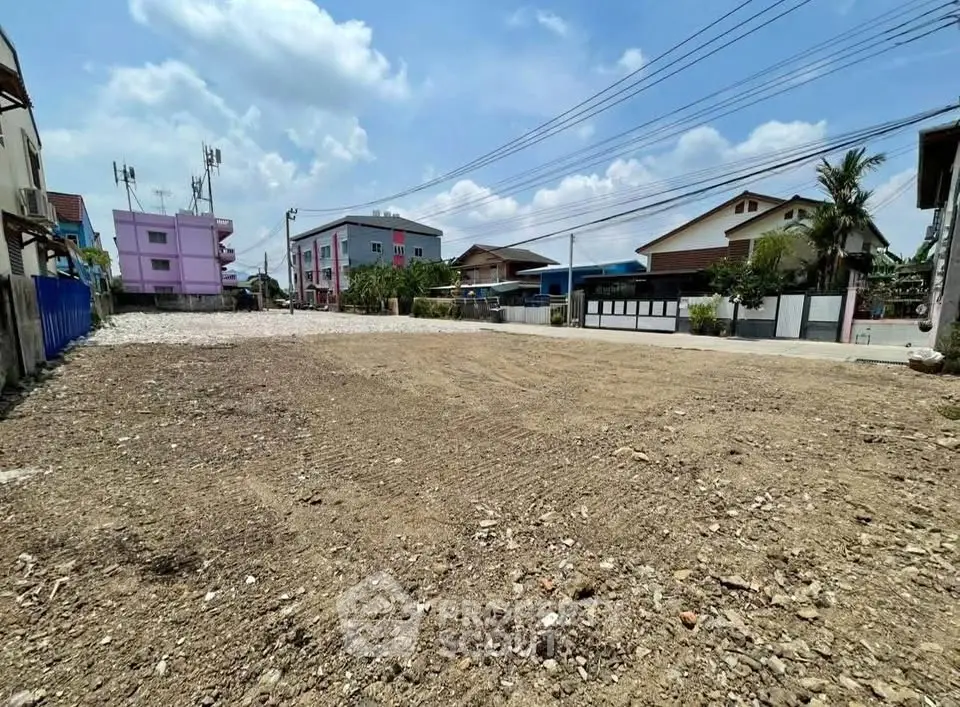 Spacious vacant land plot in a residential area with clear skies and surrounding houses.