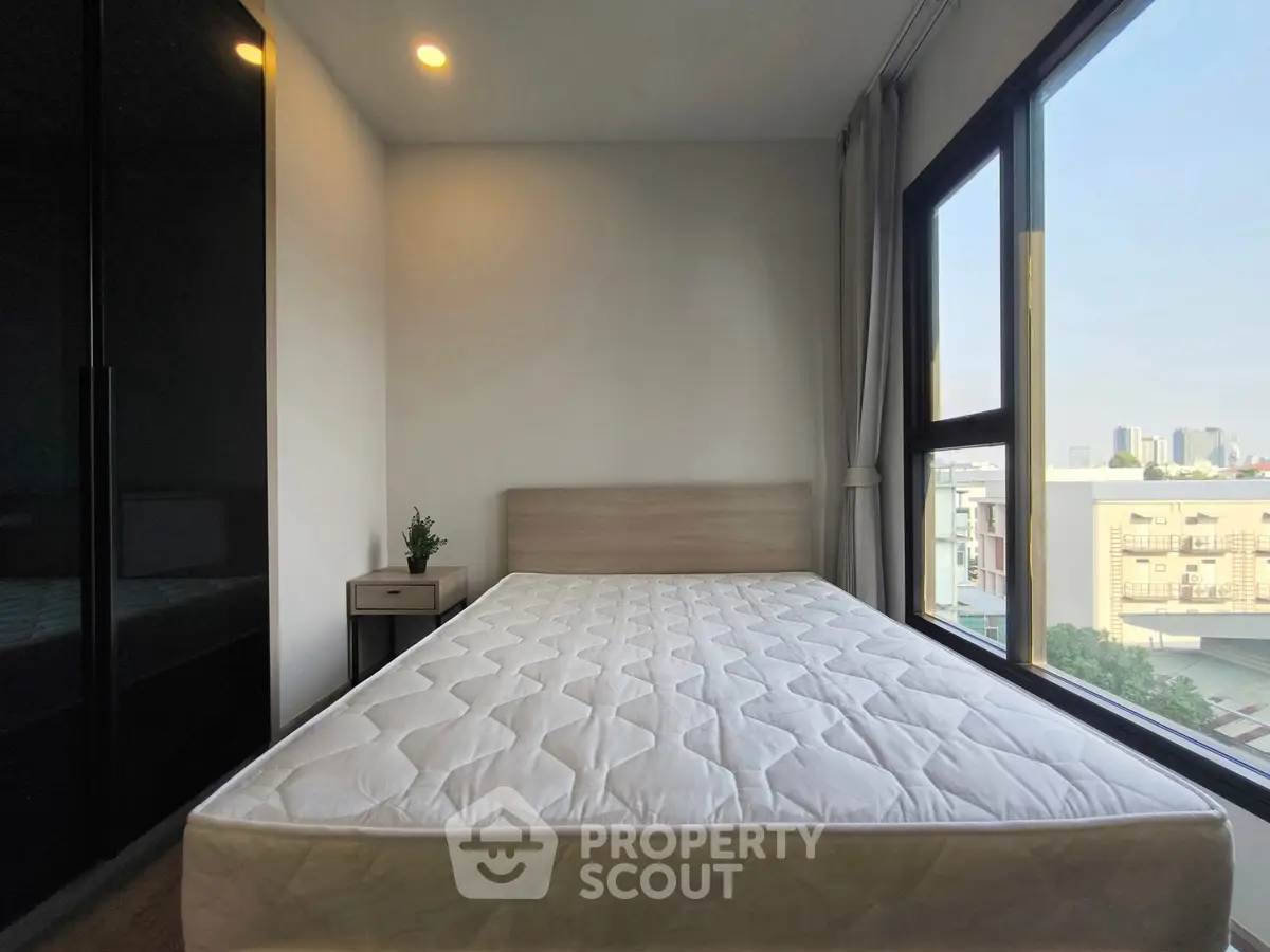 Modern bedroom with large window and city view, featuring a comfortable bed and sleek design.