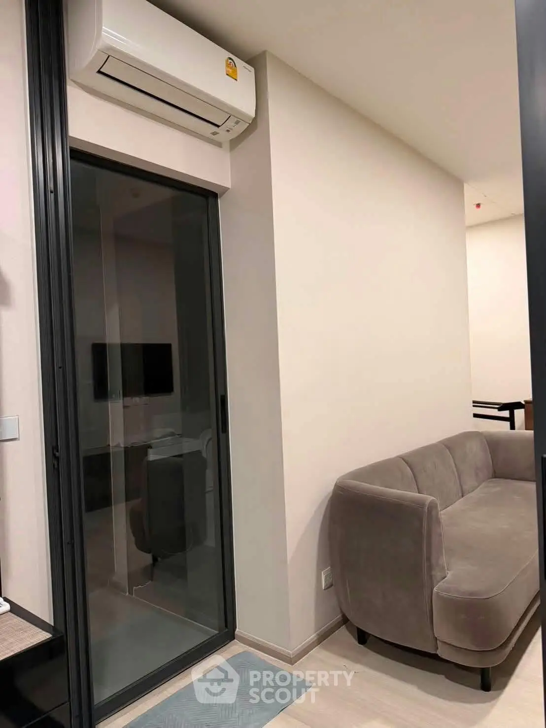 Modern living room with sleek glass door and cozy gray sofa, featuring a wall-mounted air conditioner.