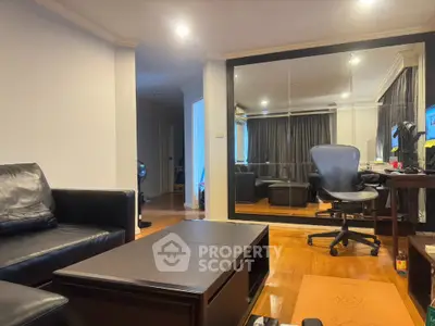 Modern living room with leather sofa and ergonomic chair, featuring mirrored wall and wooden flooring.