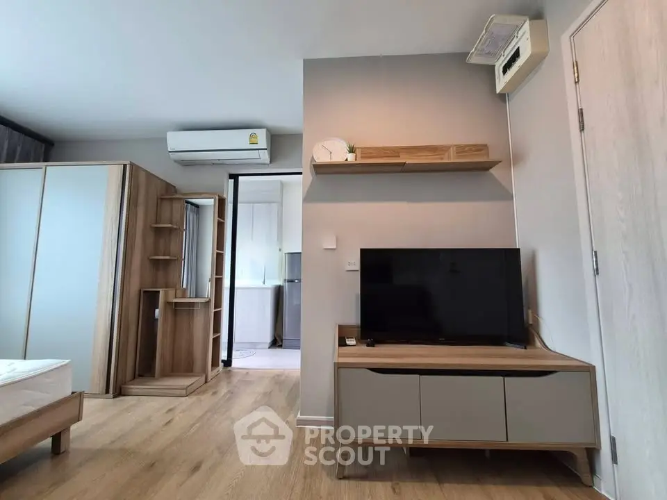 Modern living room with wooden flooring, sleek TV stand, and air conditioning unit in a stylish apartment.