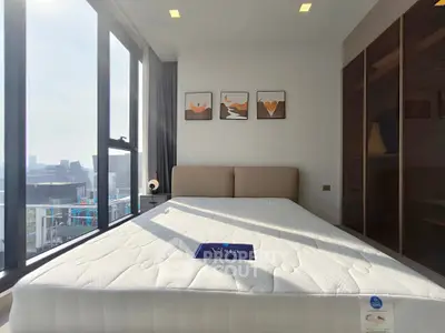 Modern bedroom with large windows and city view, featuring a cozy bed and stylish decor.