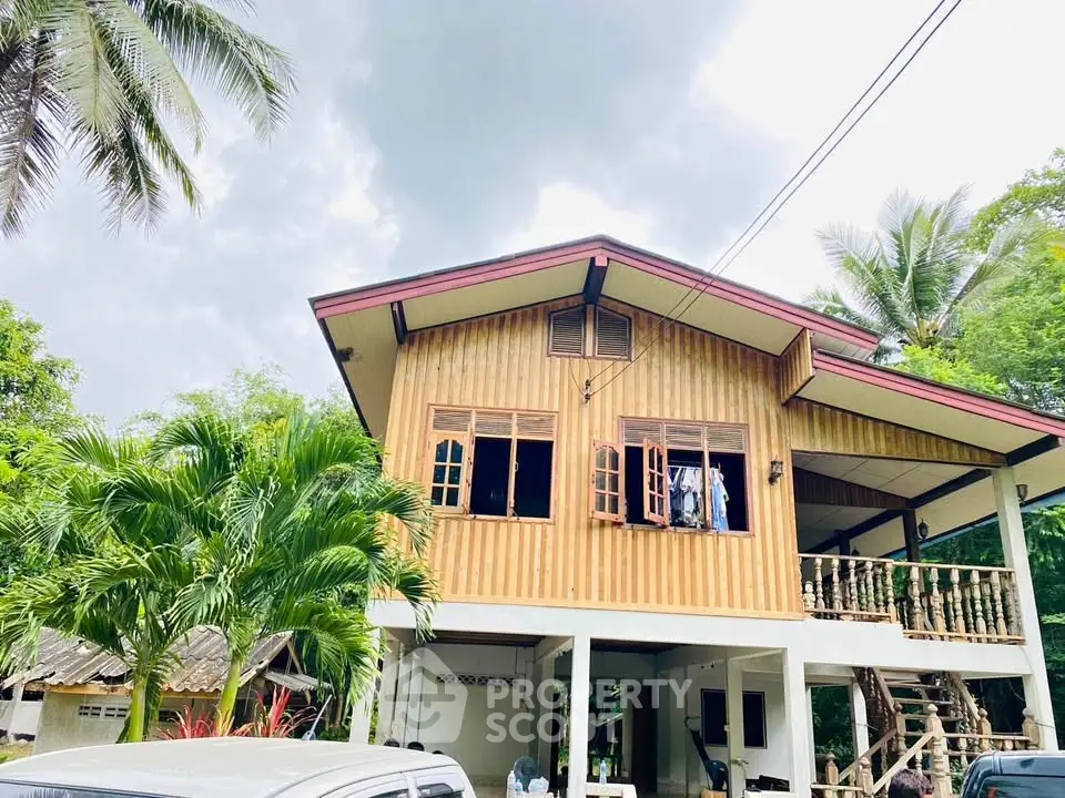 Charming two-story wooden house with lush greenery and tropical palm trees.