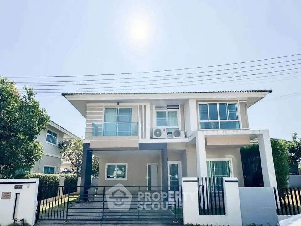 Modern two-story house with balcony and gated entrance in sunny neighborhood.
