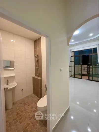 Modern apartment interior with bathroom and spacious living area leading to balcony.