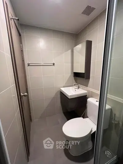 Modern bathroom with sleek fixtures and neutral tiles, featuring a compact vanity and toilet.
