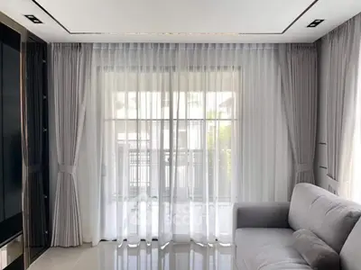 Elegant living room with large windows and sheer curtains, featuring a modern gray sofa and glossy tiled floor.