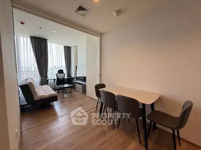 Modern living room with dining area and city view, featuring sleek furniture and large windows.